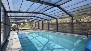 Una piscina techada con pared de piedra y sillones de descanso.