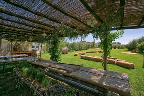 En utomhusplats med en pergola, picknickbord, höbalar och ett litet förråd.