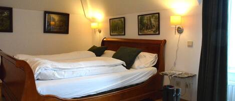 A wooden bed with white linens and green pillows, two wall-mounted lamps, and a small table with a lamp.