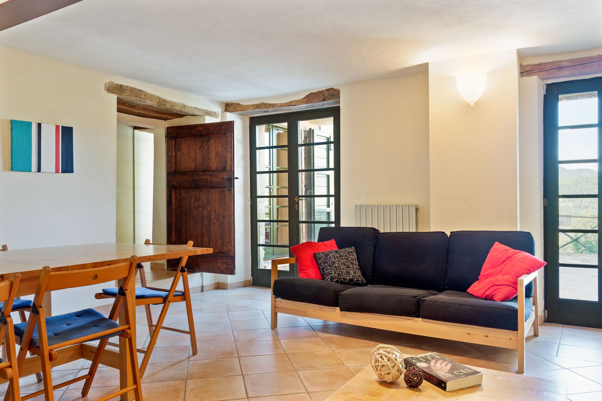 A cozy living area with a wooden sofa, a dining table with chairs, and a large window providing natural light.
