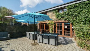 An outdoor patio with a table and chairs, a blue umbrella, and a stone wall.