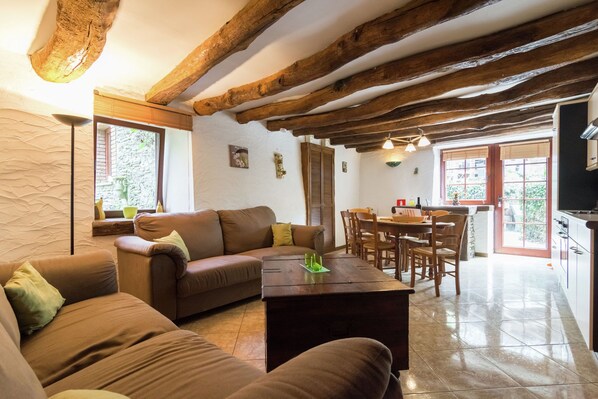A cozy living room with a brown sofa, wooden beams on the ceiling, a dining area with a table and chairs, and a kitchen area with cabinets and a stove. - Quaint Apartment in Sensenruth with Terrace (Sensenruth)
