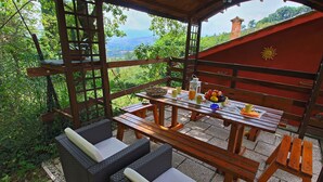 Une terrasse extérieure en bois, avec une table dressée pour les repas, entourée de meubles en osier, et offrant une vue sur un paysage verdoyant et luxuriant.