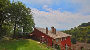 Une maison rouge avec un toit en tuiles et des cheminées, entourée d’une pelouse et d’arbres.