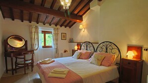 Une chambre à coucher avec un grand lit, des tables de chevet avec des lampes, un bureau en bois avec un miroir et une fenêtre avec des rideaux.