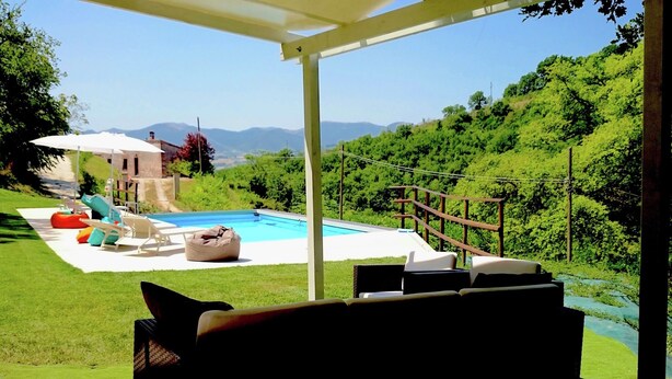 Un espace piscine offrant une vue sur un paysage montagneux, entouré de verdure et équipé de chaises longues et d’un barbecue.