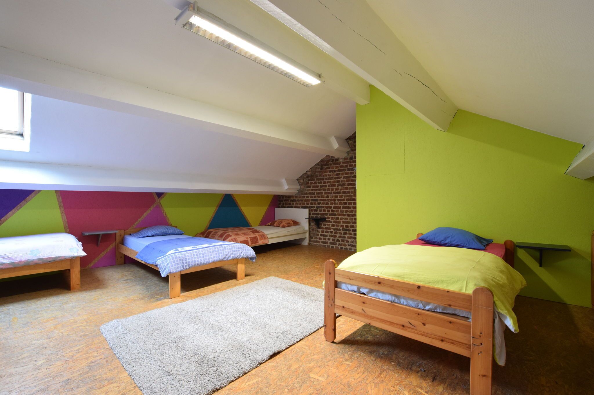Een slaapzaal met drie houten bedden, een bakstenen muur en een schuin dak met dakramen.