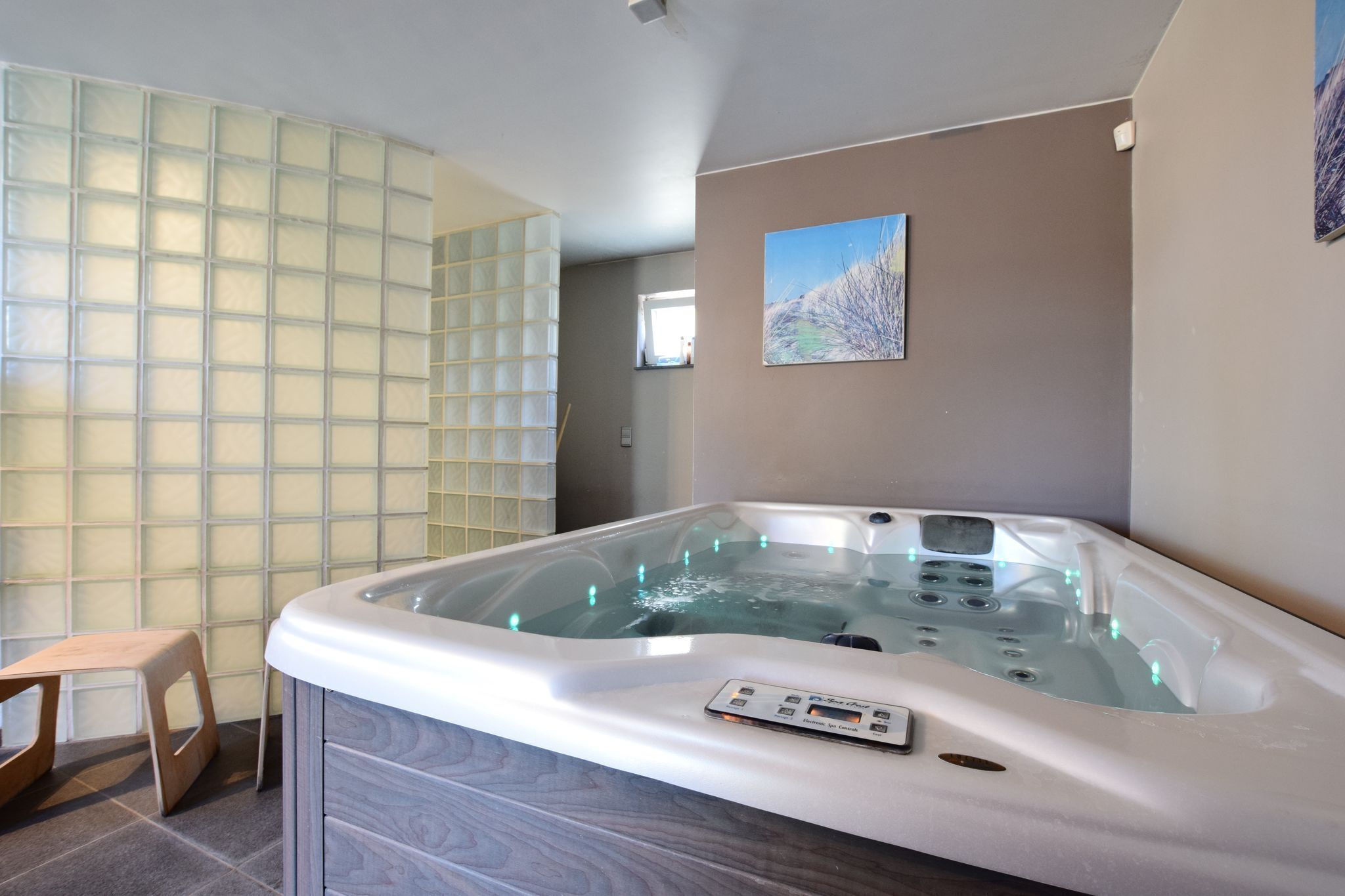 A modern bathroom with a large bathtub, a wooden stool, and a glass partition wall.