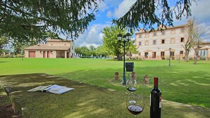 A table with a bottle of wine and glasses, set on a grassy lawn with a building in the background.