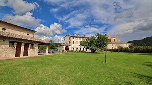 A large, historic building with a courtyard, surrounded by lush greenery and a clear sky.