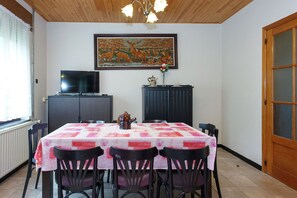 A dining area with a table set for four, a television on a cabinet, and a painting on the wall. - Quaint Holiday Home with Fenced Garden in Manhay (Dochamps)