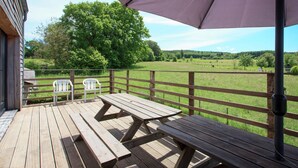 A wooden deck with picnic tables and chairs, overlooking a grassy field and trees. - Stunning Cottage with Terrace in Manhay (Vaux-Chavanne)