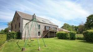 A large, rustic house with a wooden exterior, a green swing set in the yard, and a well-maintained lawn. - Stunning Cottage with Terrace in Manhay (Vaux-Chavanne)