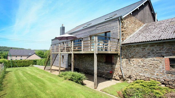 A two-story stone building with a wooden deck and a covered outdoor seating area. - Stunning Cottage with Terrace in Manhay (Vaux-Chavanne)