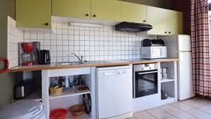 Een compacte keuken met een vaatwasser, magnetron en oven. Boven het aanrecht bevinden zich kastjes en een spoelbak.