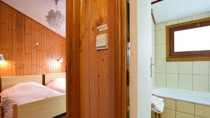 Een kamer met houten lambrisering, een bed, een raam en een badkamer met een bad.