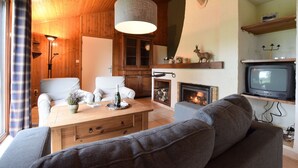 A cozy living room with wooden walls, a fireplace, a television, and a sofa.