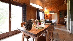 A wooden dining area with a table set for four, a large window, and a kitchen in the background.