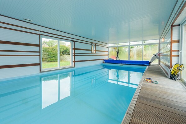 Une piscine intérieure avec des parois en verre transparent, une terrasse en bois et un escalier bleu pour accéder à la piscine.