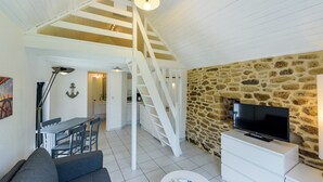 A modern living room with a staircase, a stone wall, a flat-screen TV, and a dining area. - Holiday home with private pool (Plouguin)