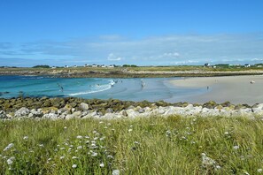 A coastal beach with a rocky shoreline, grassy areas, and houses in the background. - Holiday home with private pool (Plouguin)
