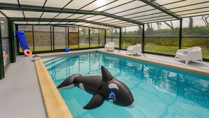 A covered swimming pool with a shark float, white lounge chairs, and a view of the outdoors. - Holiday home with private pool (Plouguin)