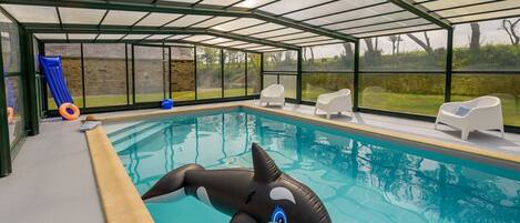 Ein überdachter Pool mit einem Haifisch-Schwimmpfad, weißen Liegestühlen und Blick ins Freie.