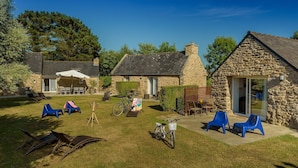 A stone building with a thatched roof, a patio with chairs, and a bicycle. - Holiday home with private pool (Plouguin)