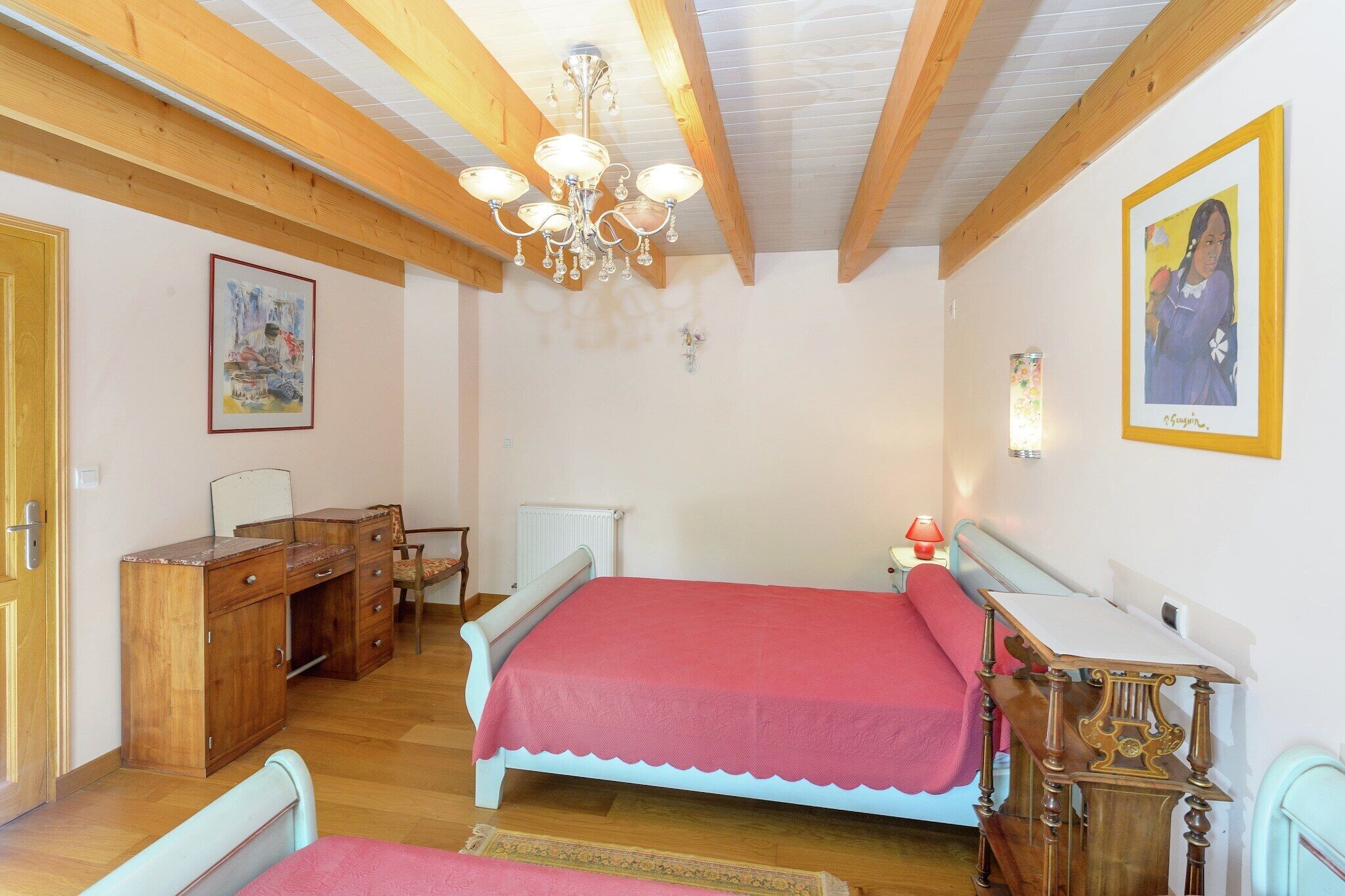 Ein Schlafzimmer mit Holzboden, einem Bett mit rosa Bettdecke, einem hölzernen Schminktisch, einem Schreibtisch und einem Stuhl.