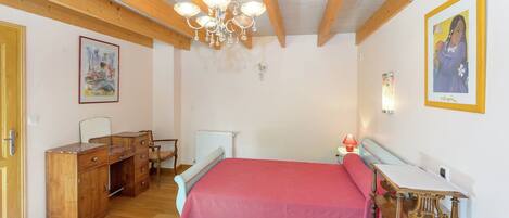 Ein Schlafzimmer mit Holzboden, einem Bett mit rosa Bettdecke, einem hölzernen Schminktisch, einem Schreibtisch und einem Stuhl.