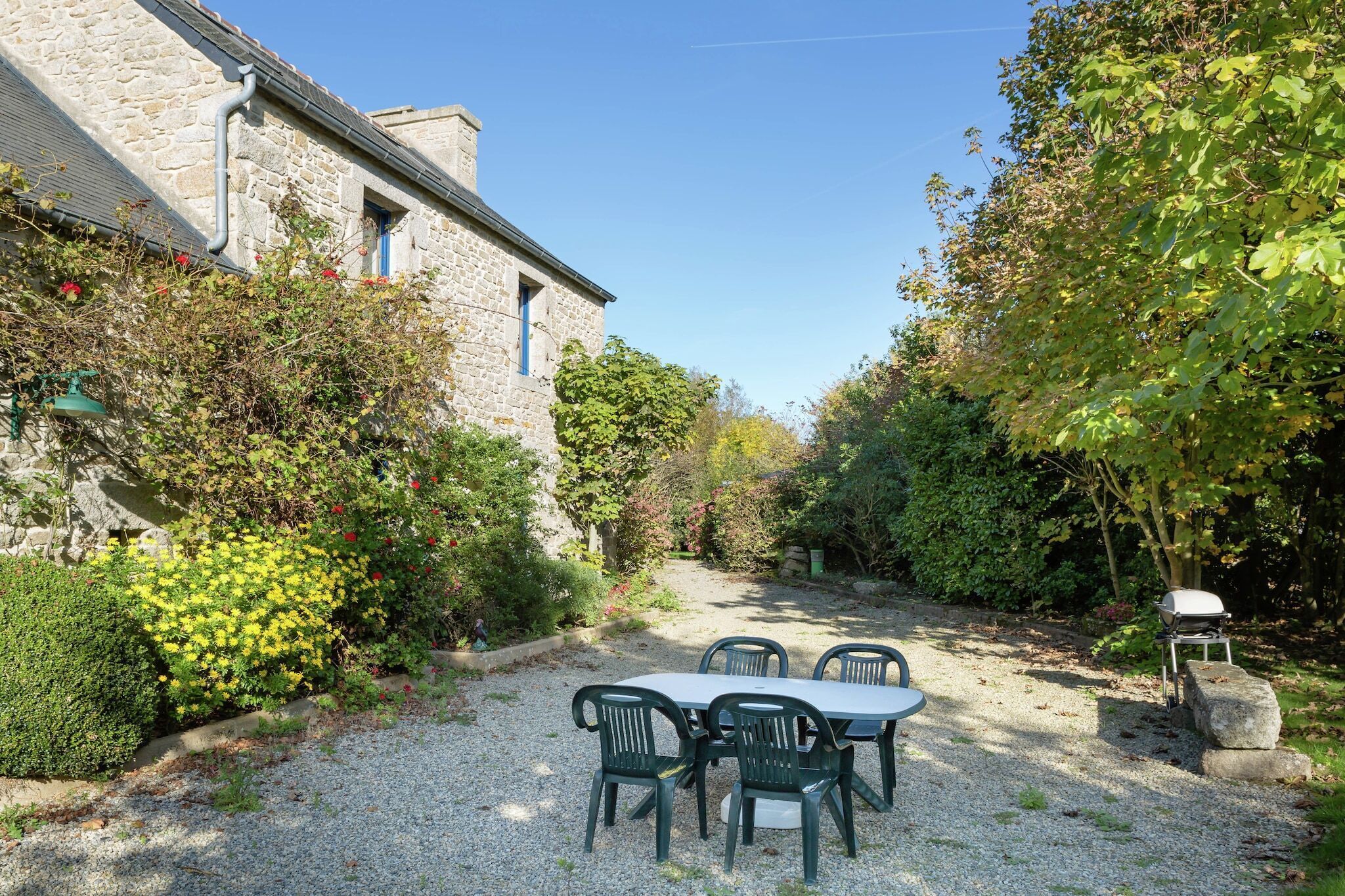 Un bâtiment en pierre avec un chemin de gravier menant à une table et à des chaises.