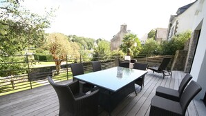 Une terrasse extérieure couverte, avec une table rectangulaire et six chaises en osier.