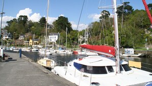 Un port de plaisance avec plusieurs bateaux amarrés, un ciel dégagé et des bâtiments en arrière-plan.