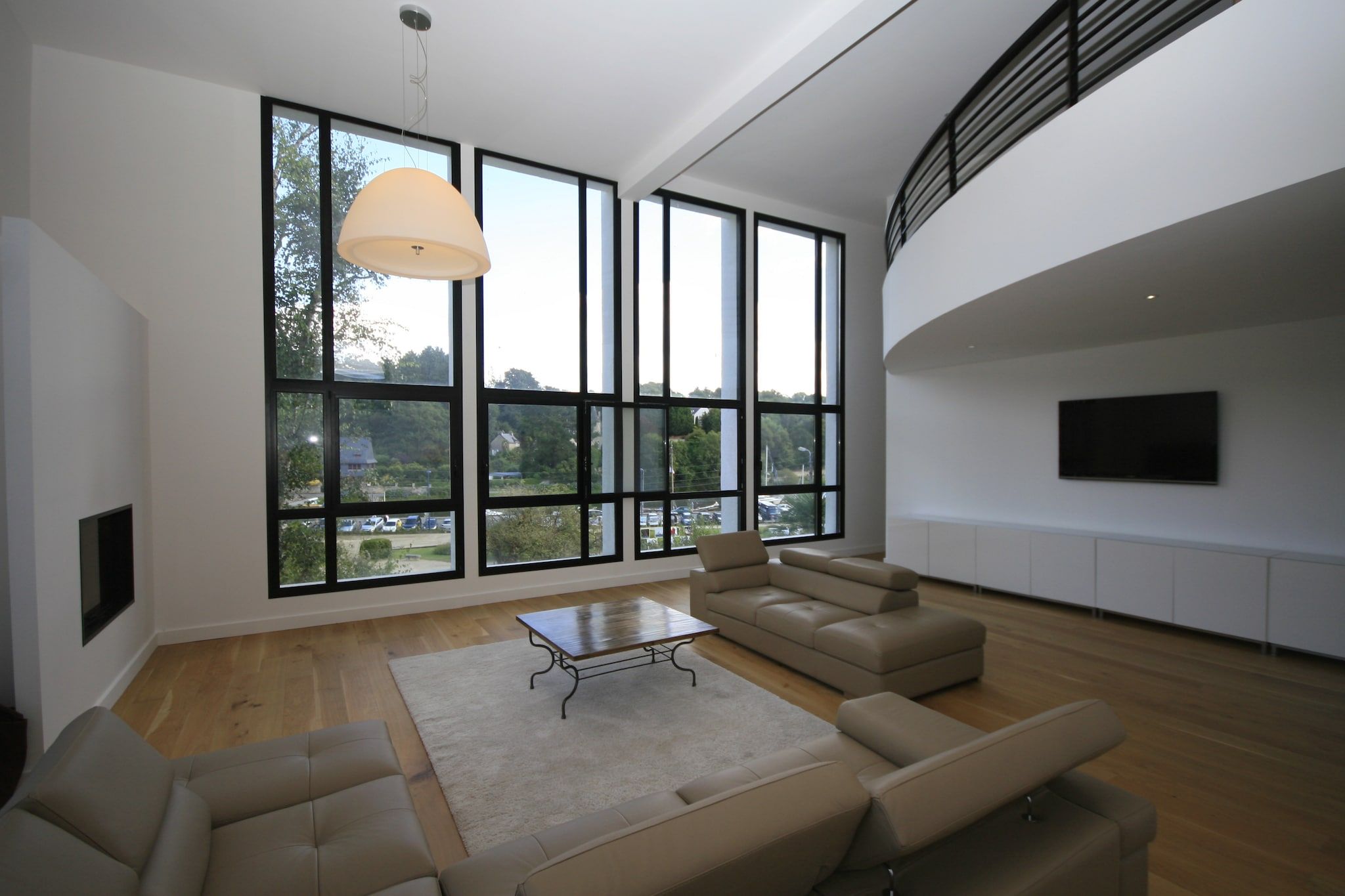 A spacious living room with large windows, a flat-screen TV, and a modern sofa set.