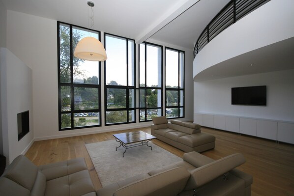 A spacious living room with large windows, a flat-screen TV, and a modern sofa set.