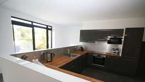 Une cuisine moderne dotée d’un plan de travail en bois, d’appareils électroménagers en acier inoxydable et d’armoires de couleur sombre.
