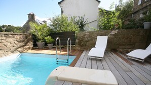 Une terrasse en bois avec une piscine, des chaises longues et des plantes en pot.