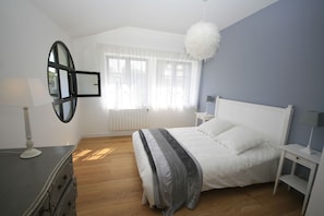 Une chambre à coucher comprenant un lit, une commode, une table de chevet, un miroir et une fenêtre avec des rideaux.