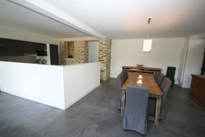 Une cuisine moderne avec un mur d’accent en pierre, un coin repas avec une table en bois et des chaises à revêtement gris, ainsi qu’un luminaire suspendu.