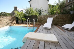 A swimming pool with a wooden deck, two lounge chairs, and a metal ladder.