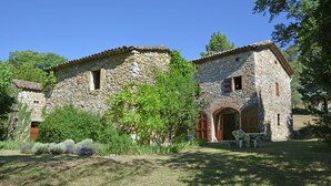 A stone building with a tiled roof, an arched doorway, and a small patio area with outdoor furniture. - Villa in Bagard with Garden, BBQ, Garden Furniture, Playroom (Bagard)