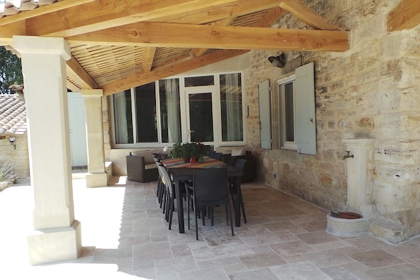 An outdoor patio area with a stone floor, wooden pergola, and a dining table with chairs.