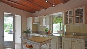 A kitchen with white cabinets, a wooden table, and a window with a view of greenery. - Two guest houses with private pool (Saint Privas de Champclos)