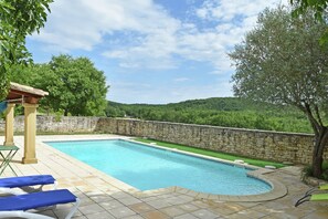 A swimming pool with a stone wall and a view of a forested hillside.