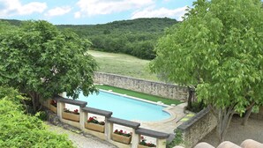 A swimming pool with a stone wall and flower planters, surrounded by lush greenery and trees. - Two guest houses with private pool (Saint Privas de Champclos)