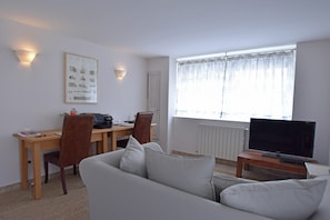 A living room with a sofa, a TV, a desk with a computer, and a window with curtains.