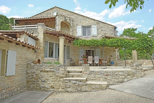 A stone house with a porch, a small garden, and a clear sky.