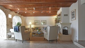 A cozy living room with a stone wall, wooden ceiling, and a fireplace. There are two armchairs, a sofa, and a coffee table. - Two guest houses with private pool (Saint Privas de Champclos)