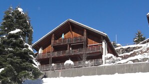 Un chalet en bois doté de balcons, entouré d’arbres couverts de neige et surplombant un ciel bleu clair.