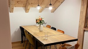 Un coin repas avec une table en bois, des chaises, un vase de fleurs et des luminaires suspendus.